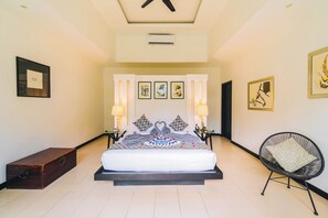 Quarto de hotel com uma cama grande, duas luminárias de cabeceira, uma cômoda, uma mesinha e uma cadeira.