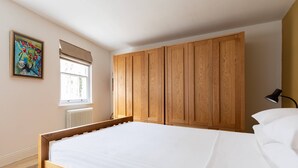 A bedroom with a wooden bed frame, a window with blinds, a radiator, and a painting on the wall. - Park Crescent Mews East II (London)