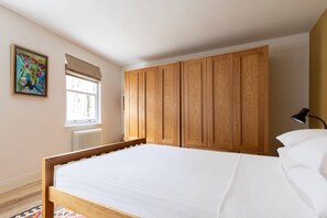 Ein Schlafzimmer mit einem hölzernen Bettgestell, einem Fenster mit Jalousien, einem Heizkörper und einem Bild an der Wand.