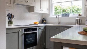 A kitchen with grey cabinets, a built-in oven, a window with potted plants, and a countertop with kitchen utensils. - Park Crescent Mews East II (London)