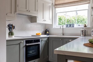 Eine Küche mit grauen Schränken, einem eingebauten Backofen, einem Fenster mit Blumentöpfen und einer Arbeitsplatte mit Küchenutensilien.
