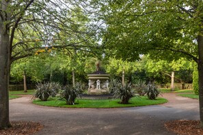 Ein Park mit einem zentralen Brunnen, umgeben von gepflegtem Rasen und Bäumen.