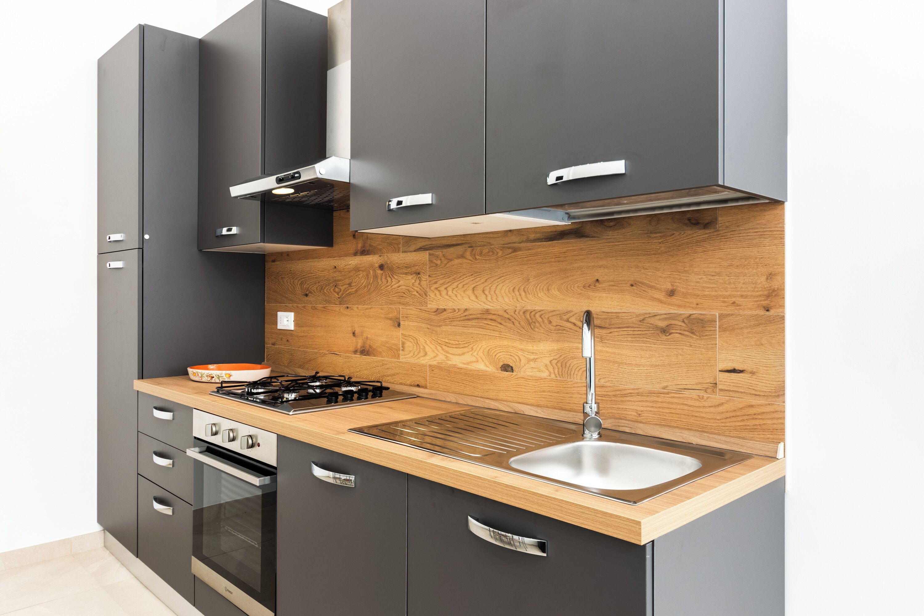 Une cuisine moderne avec des meubles de couleur sombre, un pare-feu en bois, un évier en acier inoxydable et une cuisinière à gaz.