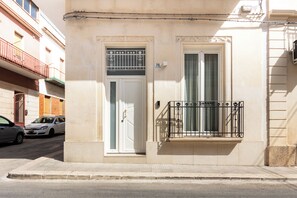 A building with a white door, a balcony with a metal railing, and a street in front. - Incanto Holiday House - Appartamento 2 (Avola)