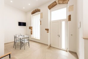 A room with a dining table, chairs, a television mounted on the wall, a door, and a window with curtains. - Incanto Holiday House - Appartamento 2 (Avola)