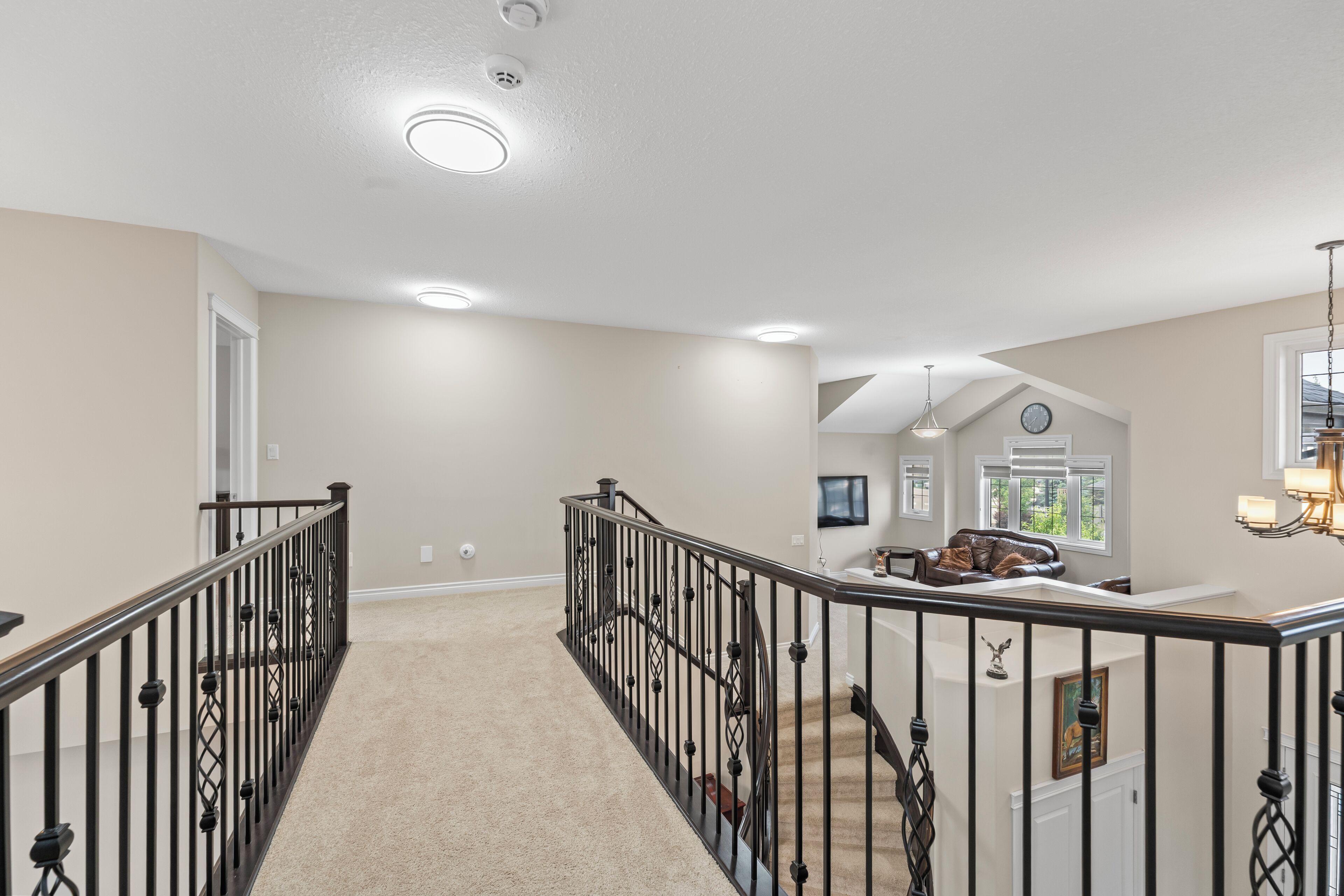 A spacious hallway with a carpeted floor, a staircase with black railings, and a living area with a couch and a television.