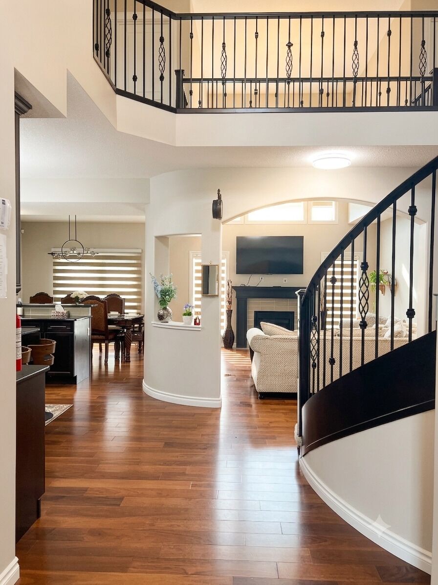 A spacious living area with a curved staircase, a fireplace, and a dining area with a chandelier.