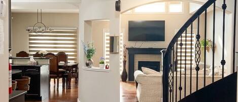 A spacious living area with a curved staircase, a fireplace, and a dining area with a chandelier.
