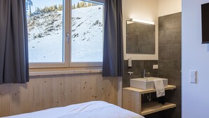 Moderni kylpyhuone, jossa on puinen allaskaappi, suuri peili ja näkymä lumiselle vuorelle.