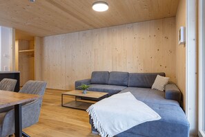 Ein modernes Wohnzimmer mit einem grauen Sofa, einem Couchtisch und einem Essbereich mit Stühlen.