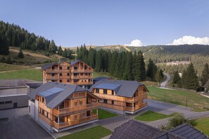 Ein modernes Holzgebäude mit mehreren Balkonen, umgeben von üppiger grüner Landschaft und einem klaren Himmel.