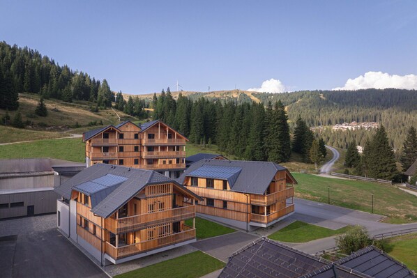 Un edificio moderno in legno con numerosi balconi, immerso in un paesaggio verdeggiante sotto un cielo sereno.