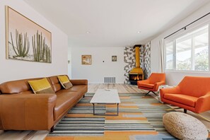 A modern living room with a brown leather sofa, a white coffee table, and orange armchairs. - Juniper & Sage Retreat - 3 bed, Pool, Spa & Stargazing Near Joshua Tree (Joshua Tree)