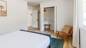 Ein Schlafzimmer mit einem Bett, einem Sessel, einem Kleiderschrank und einer Tür zu einem anderen Raum.
