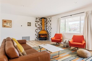 Un salon moderne avec une cheminée, un canapé en cuir marron, deux fauteuils orange et un tapis à motifs.