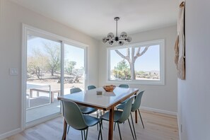 Un espace repas comprenant une table et des chaises, de grandes fenêtres offrant une vue sur un paysage désertique et un luminaire au plafond.