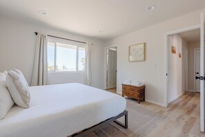 Une chambre avec un grand lit, une commode en bois et une porte donnant sur une autre pièce.