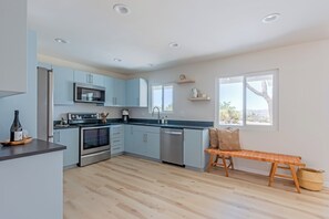 A modern kitchen with light blue cabinets, stainless steel appliances, and a wooden bench. - Juniper & Sage Retreat - 3 bed, Pool, Spa & Stargazing Near Joshua Tree (Joshua Tree)