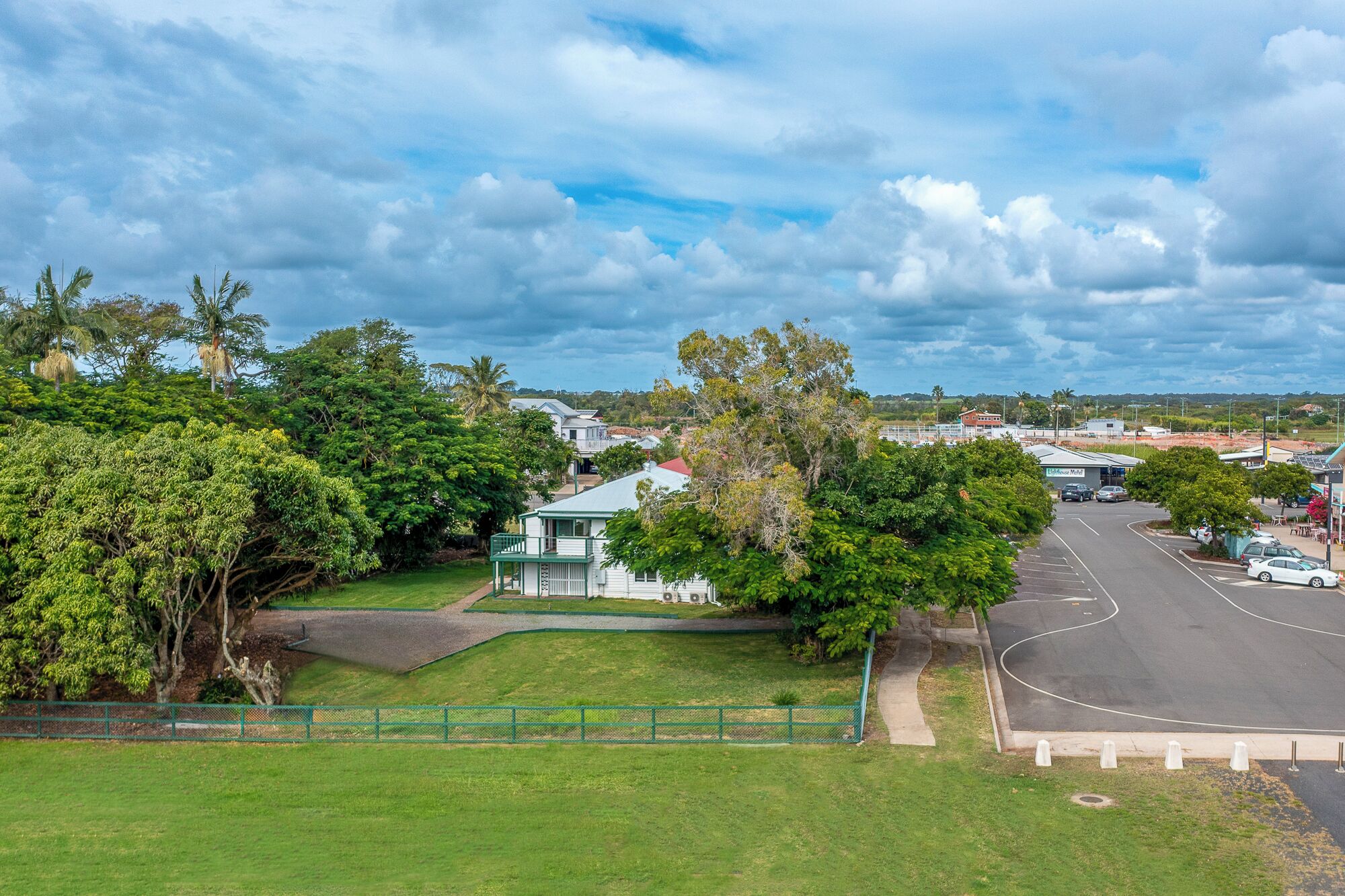 A residential area with a white house, green fence, and a road.
