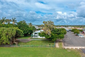 A residential area with a white house, green fence, and a road. - Ocean Soul Unit 2 (Burnett Heads)