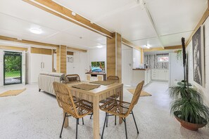 A modern kitchen with white cabinets, a dining area with a wooden table and woven chairs, and a view of a garden through a door.