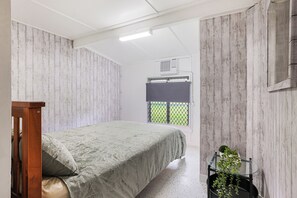 A bedroom with a bed, a wooden bench, a window with a view, and a small potted plant.