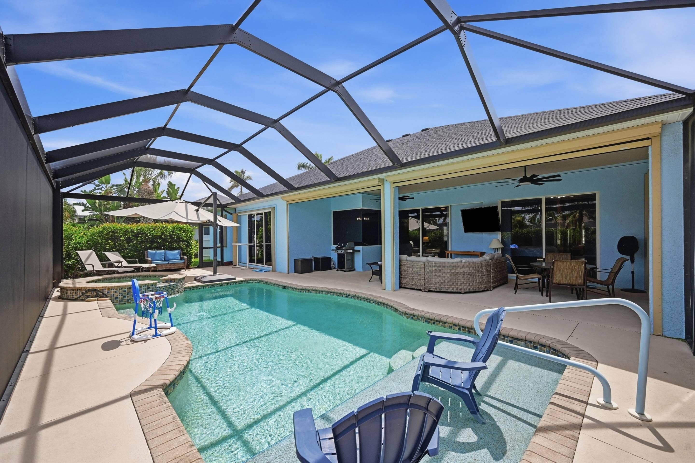 Zona de piscina con cerramiento de vidrio, sillones de descanso y comedor con mobiliario exterior.