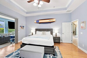 A bedroom with a bed, bedside tables, a ceiling fan, and a view of the outdoors. - Villa Cecilia | Spacious Cape Coral Escape | Private Heated Pool, Spa, Outdoor Living & Home Office (Cape Coral)
