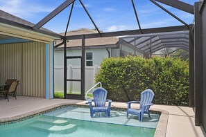 A swimming pool with two chairs, a covered patio area, and a view of a house through a screened enclosure. - Villa Cecilia | Spacious Cape Coral Escape | Private Heated Pool, Spa, Outdoor Living & Home Office (Cape Coral)