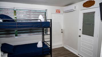 A bunk bed room with a white door, an exit sign, and a window with blinds.
