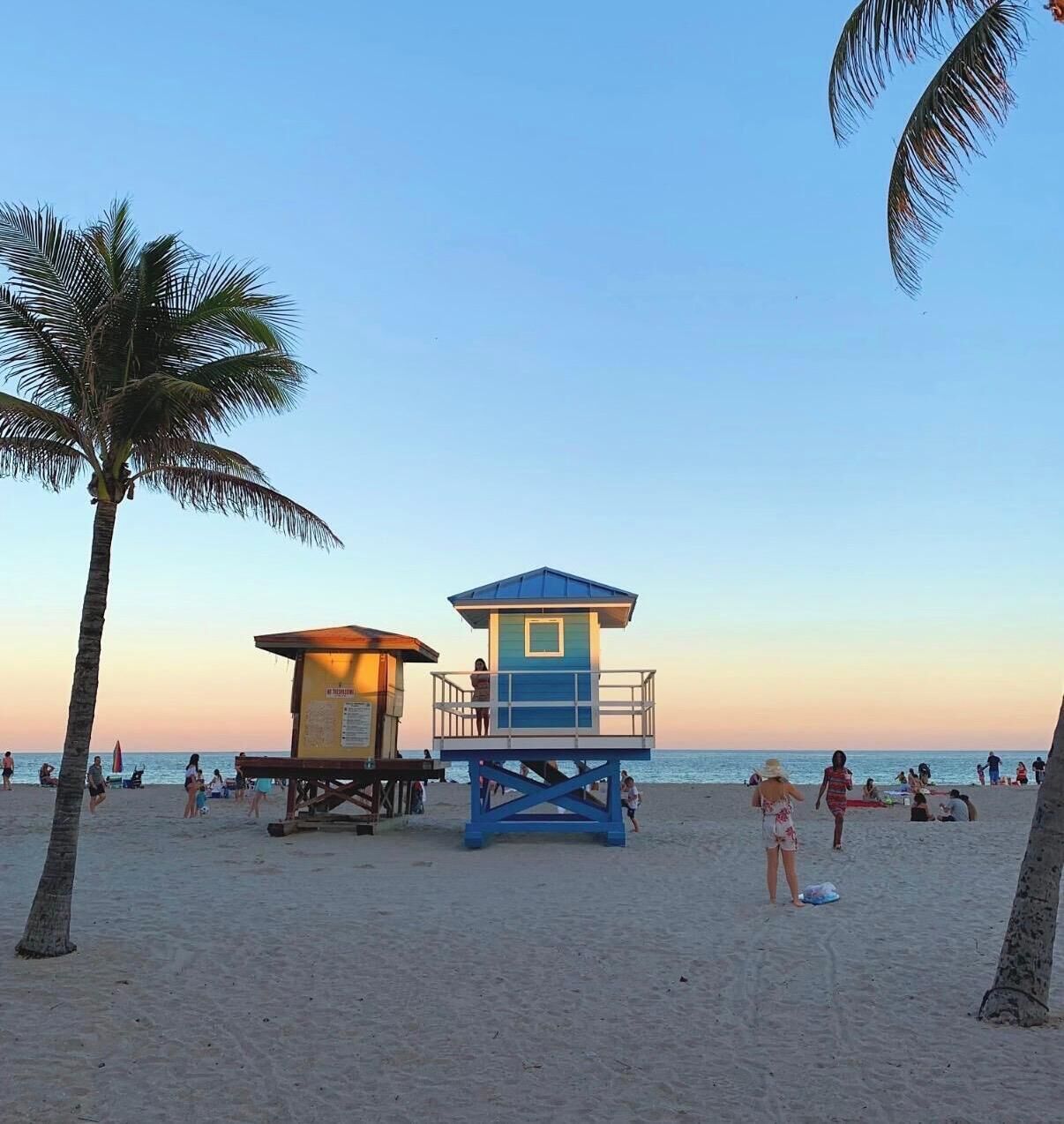 A beach with a lifeguard tower, palm trees, and people on the sand.