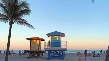 A beach with a lifeguard tower, palm trees, and people on the sand.