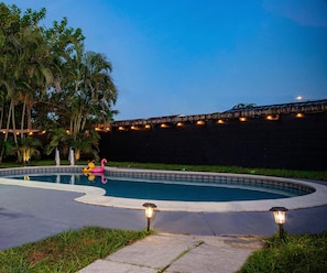 Una piscina de borde curvo, rodeada de césped y palmeras.