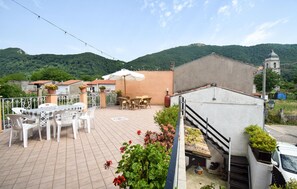 Eine Terrasse mit Gartenmöbeln, eine Treppe und Blick auf einen Hügel mit einer Kirche.