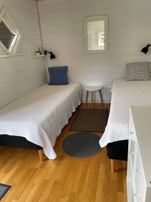 Ett litet, mysigt rum med två enkelsängar, ett litet bord, en spegel och ett fönster.
