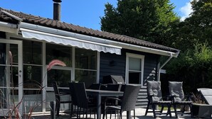 Ein überdachter Außenbereich mit Tischen, Stühlen und einem Kamin sowie einer Holzterrasse.