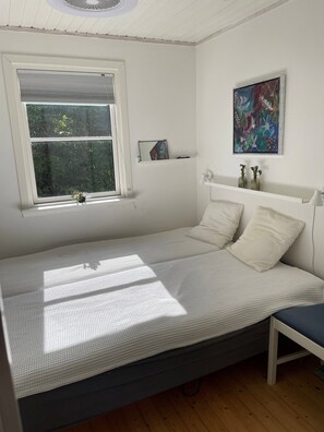 Ein Schlafzimmer mit Bett, Fenster, einem Bild und einem Nachttisch.