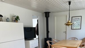 Ein moderner Wohnbereich mit Holzboden, einem Esstisch mit Stühlen, einem weißen Schrank, einem schwarzen Kamin und einer Decke mit Rastermuster.