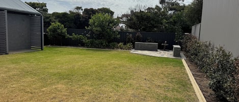 Un jardín trasero con césped, un patio de ladrillo y un área cercada con árboles y arbustos.