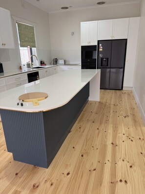 A modern kitchen with white cabinetry, a black refrigerator, and a wooden floor. - Best location with sea views. Enjoy the simple beach life with close amenities. (Victor Harbor)
