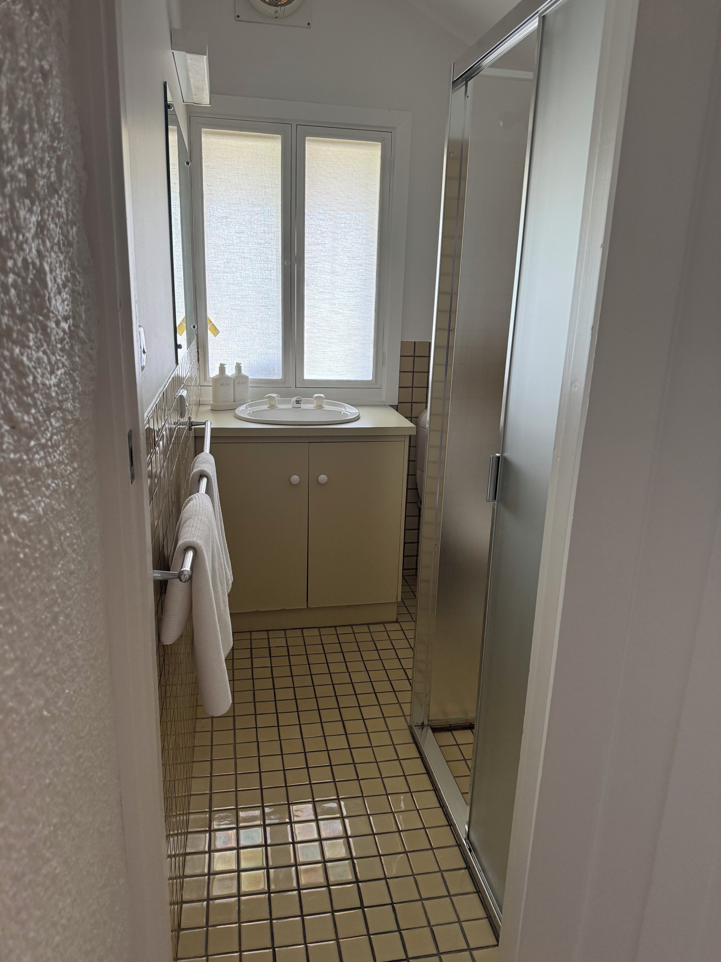 A bathroom with a tiled floor, a sink with a mirror, and a towel rack.