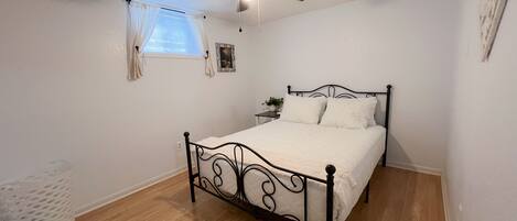 A bedroom with a bed, a ceiling fan, a window with curtains, and a bedside table with a plant.
