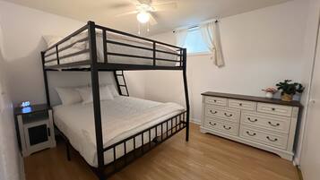 A bunk bed with a nightstand, a dresser with drawers, a ceiling fan, and a window with curtains.