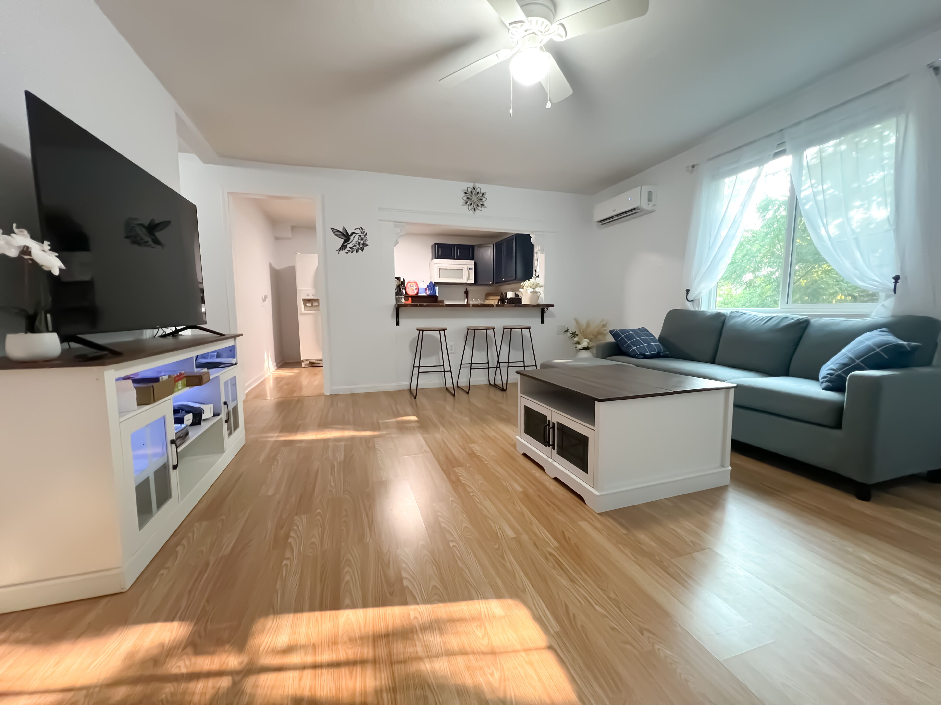 Una sala de estar moderna con un televisor de pantalla plana, un sofá gris, una mesa de centro y una cocina al fondo.