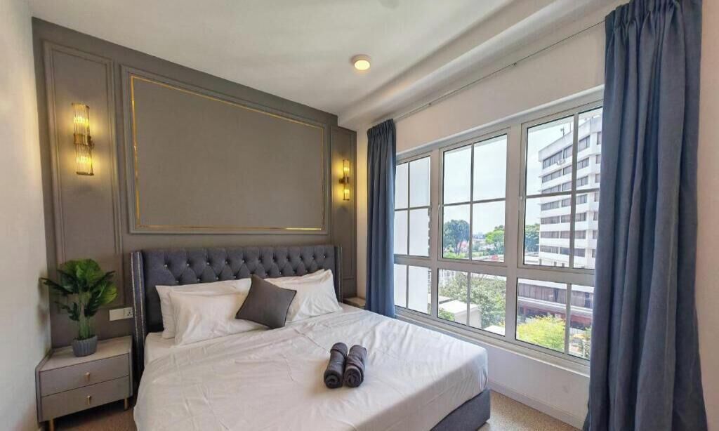 A hotel room with a large bed, a nightstand, a potted plant, and a view of buildings through the window.