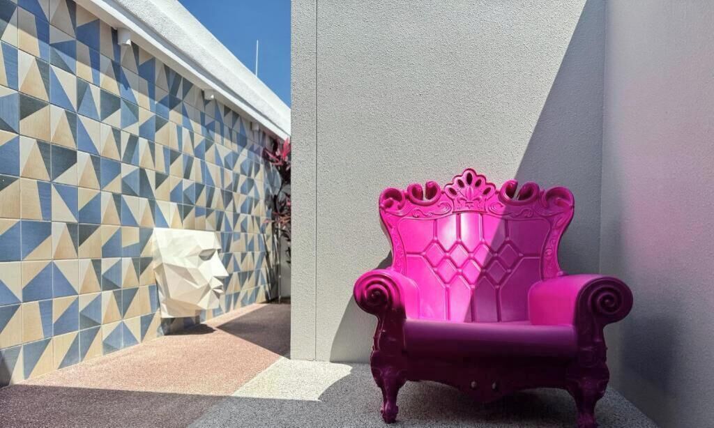 A pink chair with a crown design against a wall with a geometric pattern.