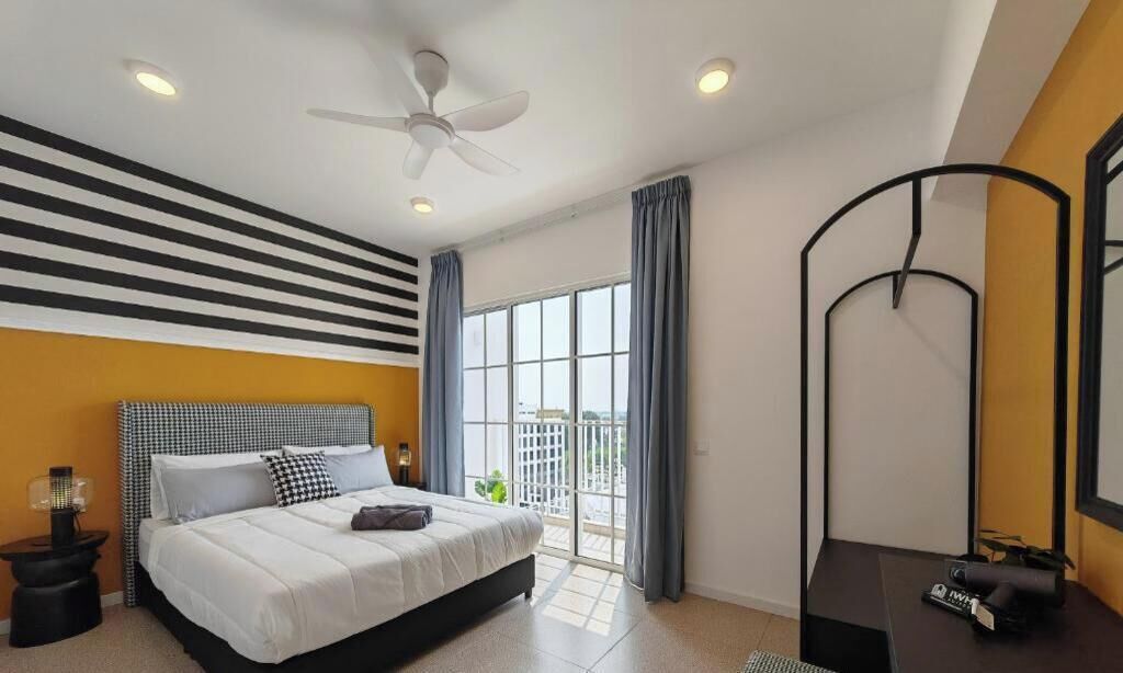 A bedroom with a bed, a ceiling fan, a nightstand, a desk, and a large window with curtains.
