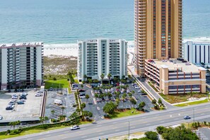 Un grand hôtel à plusieurs étages, un parking avec de nombreuses voitures et une vue sur la plage et l’océan.