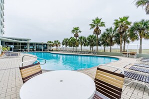 Un espace piscine avec des chaises longues et une table, entouré de palmiers.