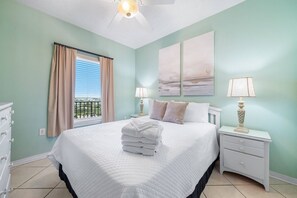 A bedroom with a bed, two bedside tables, a window with curtains, and a view of the outdoors. - Tidewater 608 | Pools + Hot Tub + Fitness (Orange Beach)